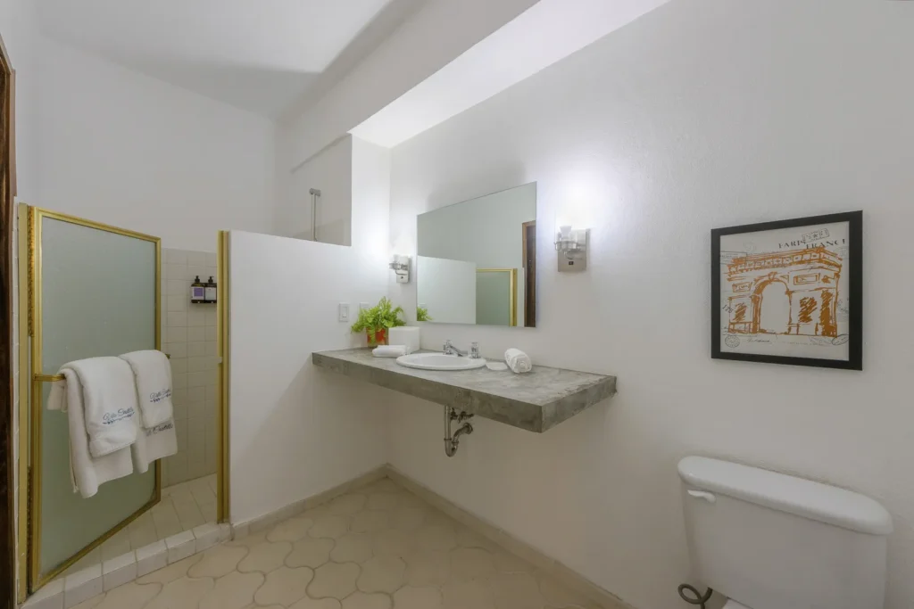 Bathroom with a concrete countertop sink, mirror, and wall-mounted lights; shower on the left with frosted glass door, towels hanging nearby, and a framed picture on the right wall