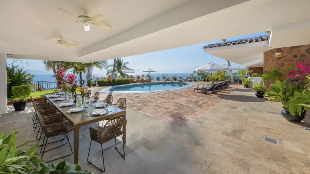 Outdoor poolside dining area with a long table set for guests and the ocean view in the background