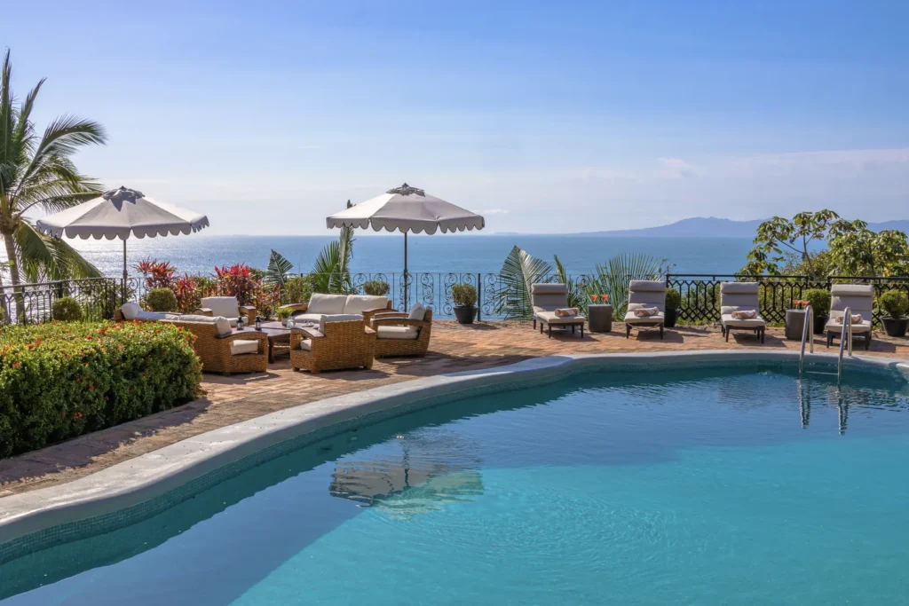 Poolside terrace with wicker seating, white umbrellas, and an ocean view.