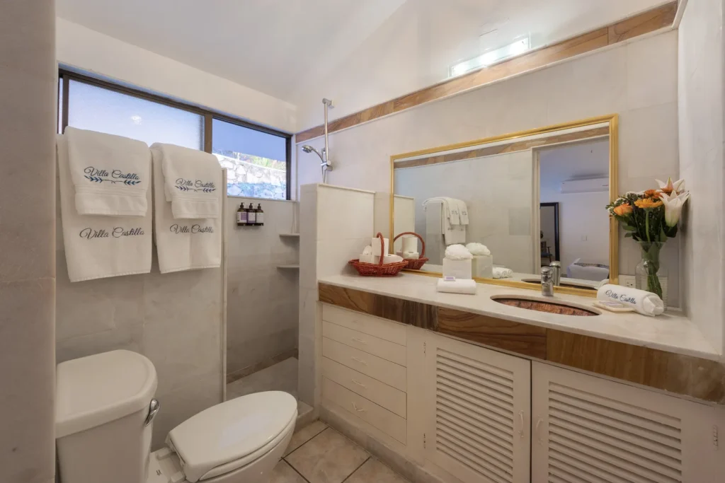 Hotel-style bathroom with a double vanity, large gold-framed mirror, and a vase of flowers on a marble countertop.