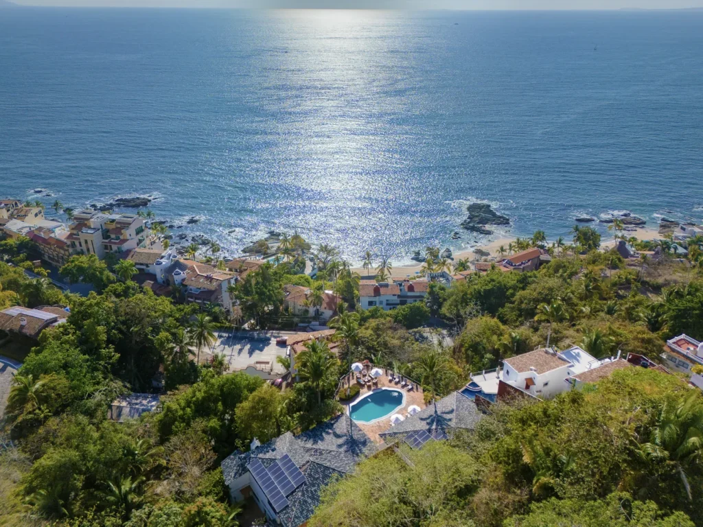 Aerial view of a tropical coastal town with a beach, palm trees, and a reflecting ocean.