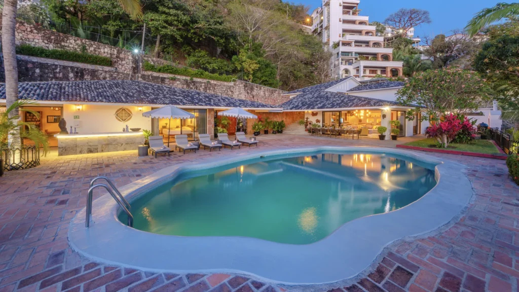 Resort pool area at dusk with lounge chairs, umbrellas, and a lit outdoor bar by the patio