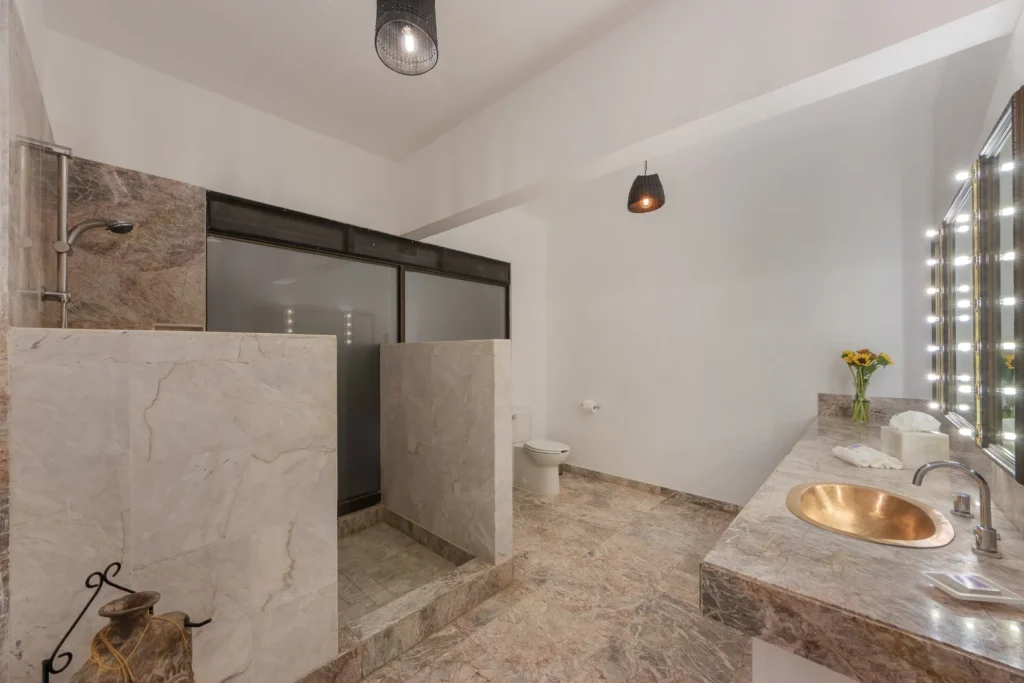 Luxurious marble bathroom with a large vanity, copper sink, and illuminated mirrors on the right.