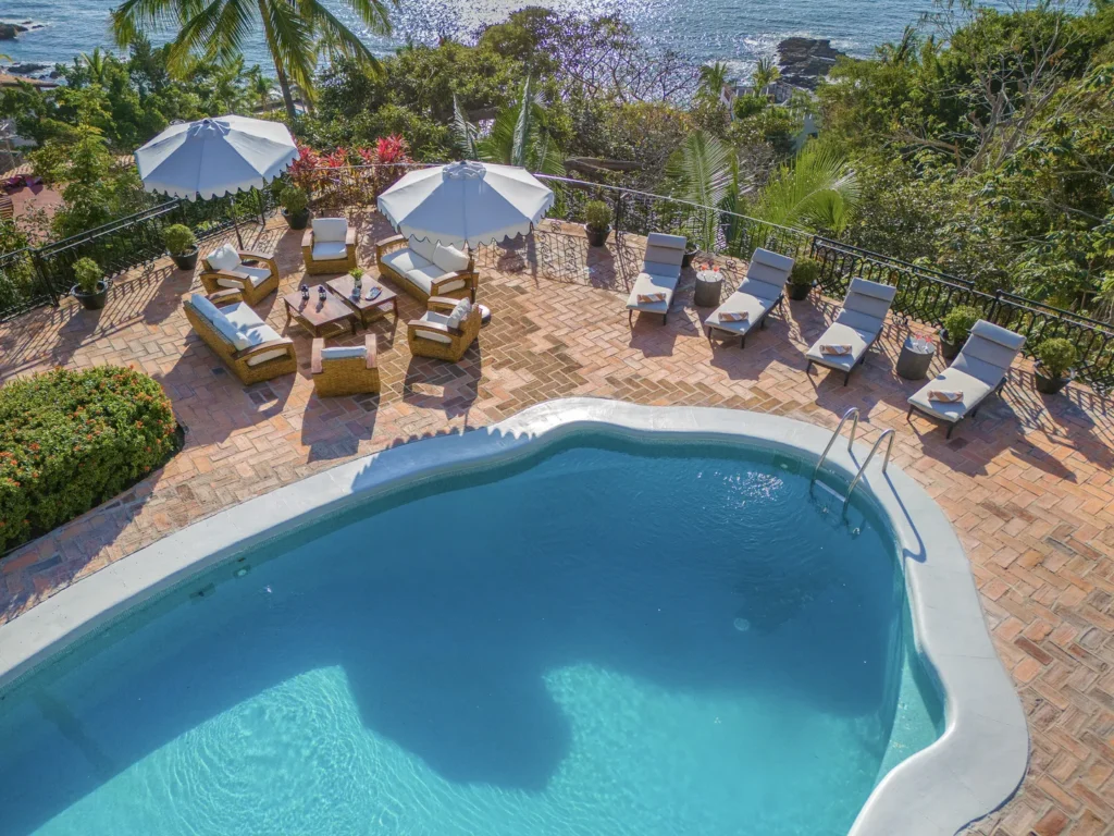 A sunny poolside patio with white-cushioned lounge chairs, wicker seating, and large umbrellas overlooking the ocean.] , should avoid error